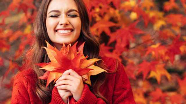 Imagen de una mujer sonriendo jugando con las hojas caídas de un árbol.