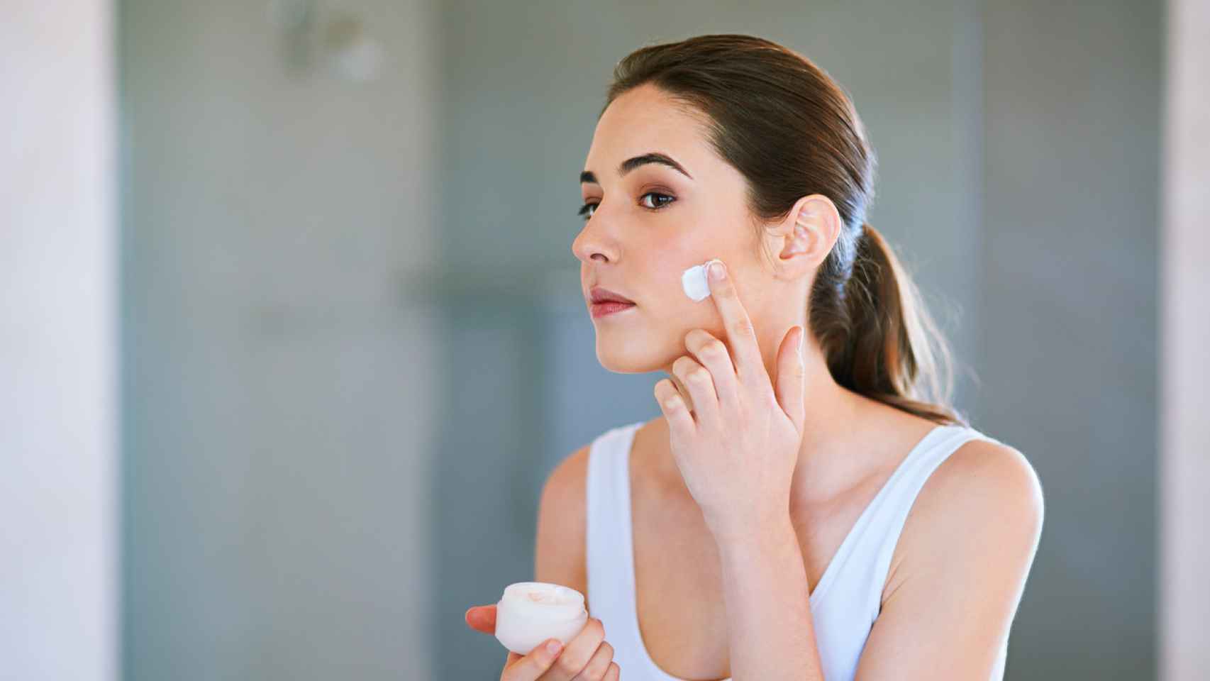 Una mujer se aplica crema hidratante en la cara.