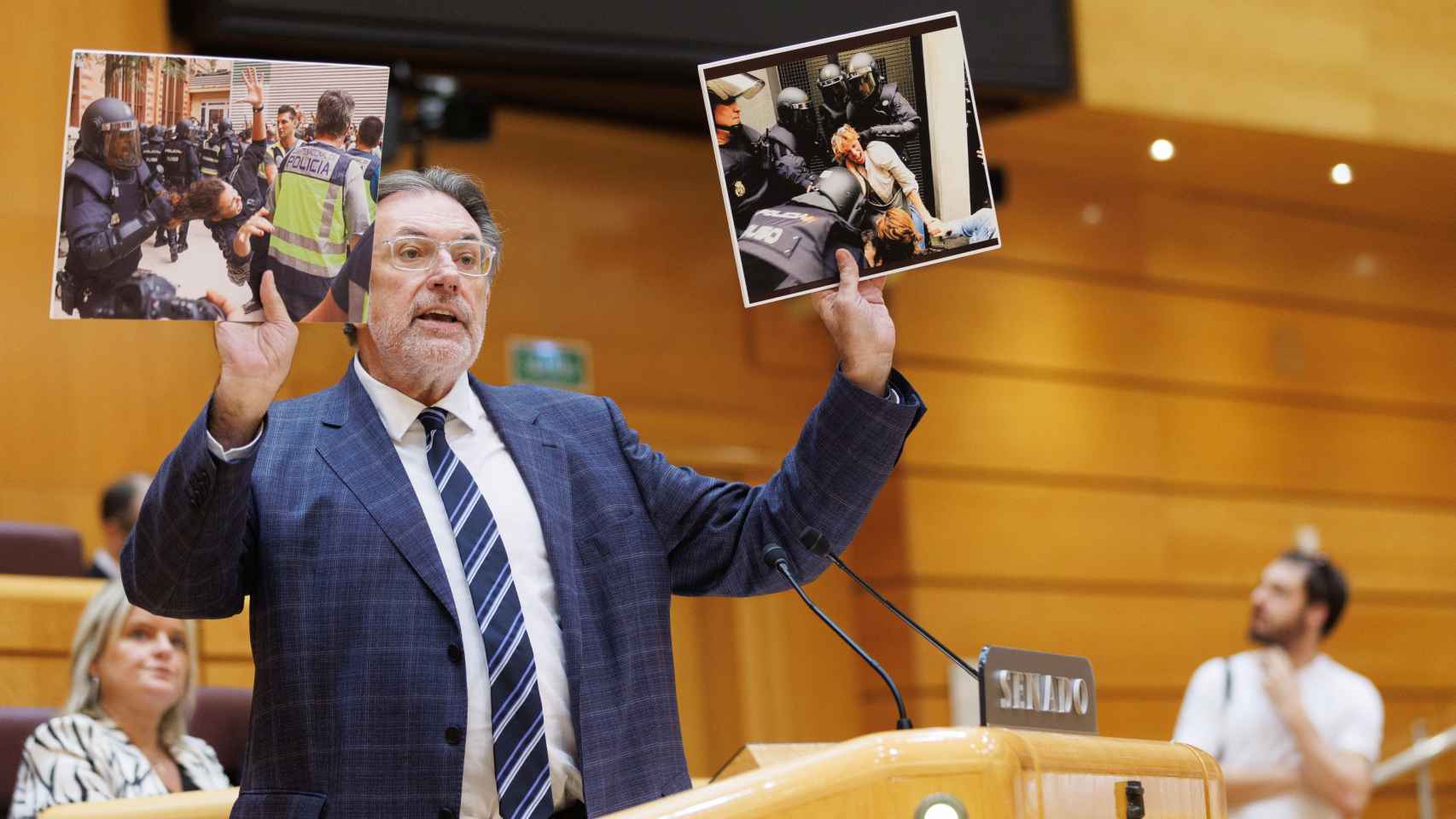 El senador de Junts Josep Lluís Cleries muestra imágenes de las cargas policiales del 1-O durante el debate.