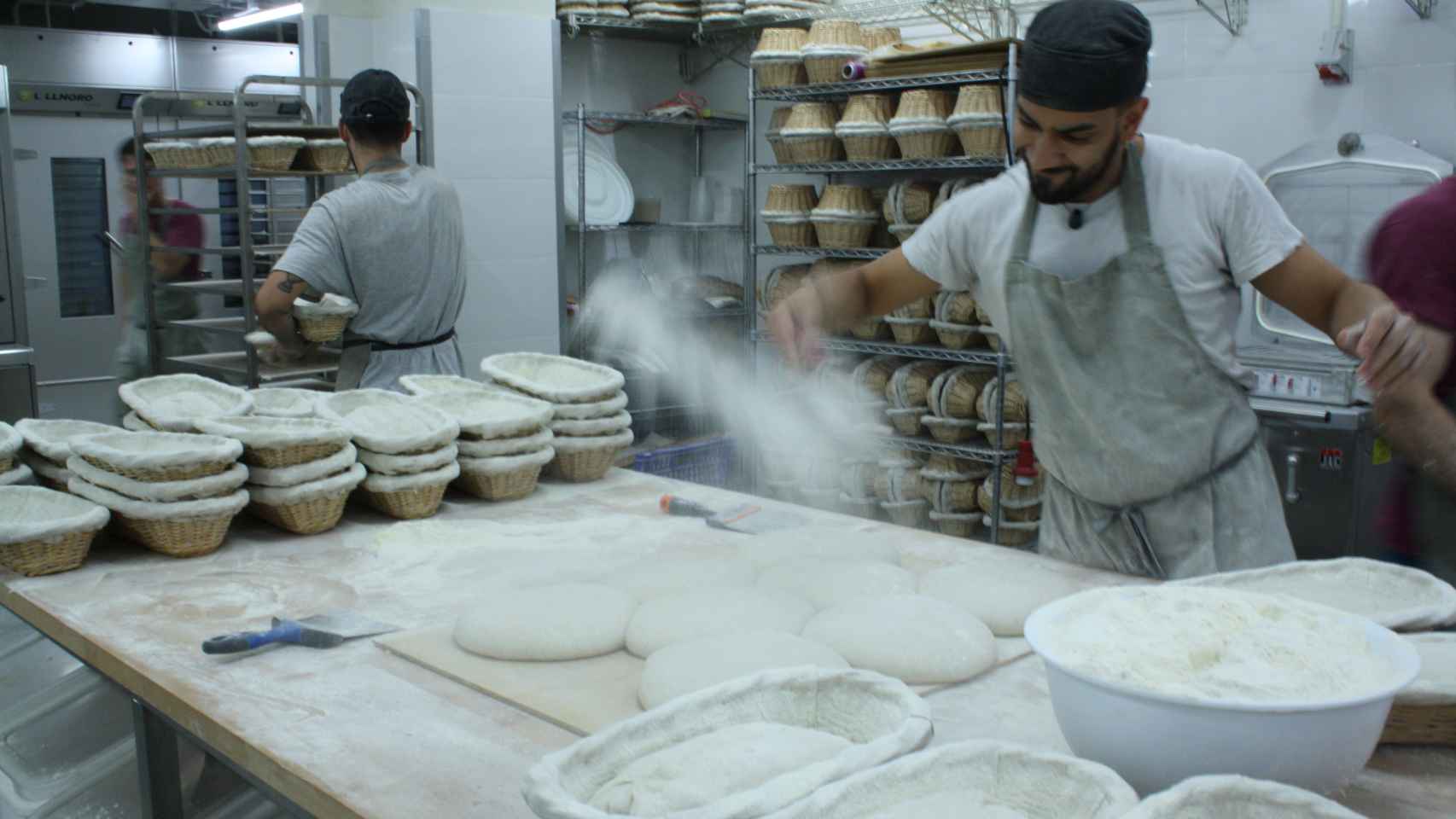 Panadero Martín esparciendo harina sobre la masa del pan en la zona de amasado.