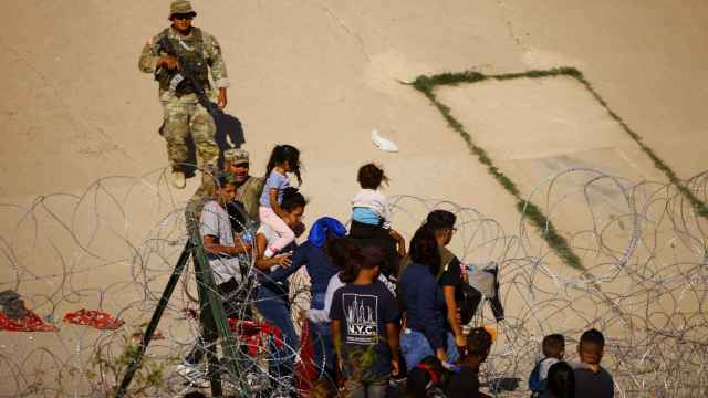 Migrantes que buscan asilo en Estados Unidos intentan cruzar una cerca de alambre de púas cerca de un muro fronterizo a orillas del río Bravo, visto desde Ciudad Juárez.