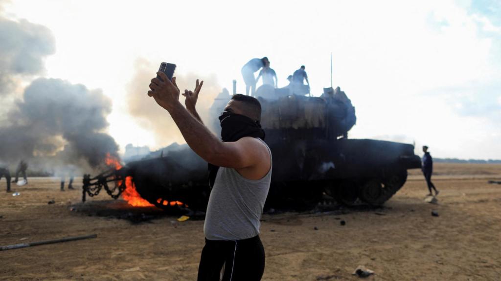 Un palestino se toma una selfie frente a un vehículo militar israelí en llamas.