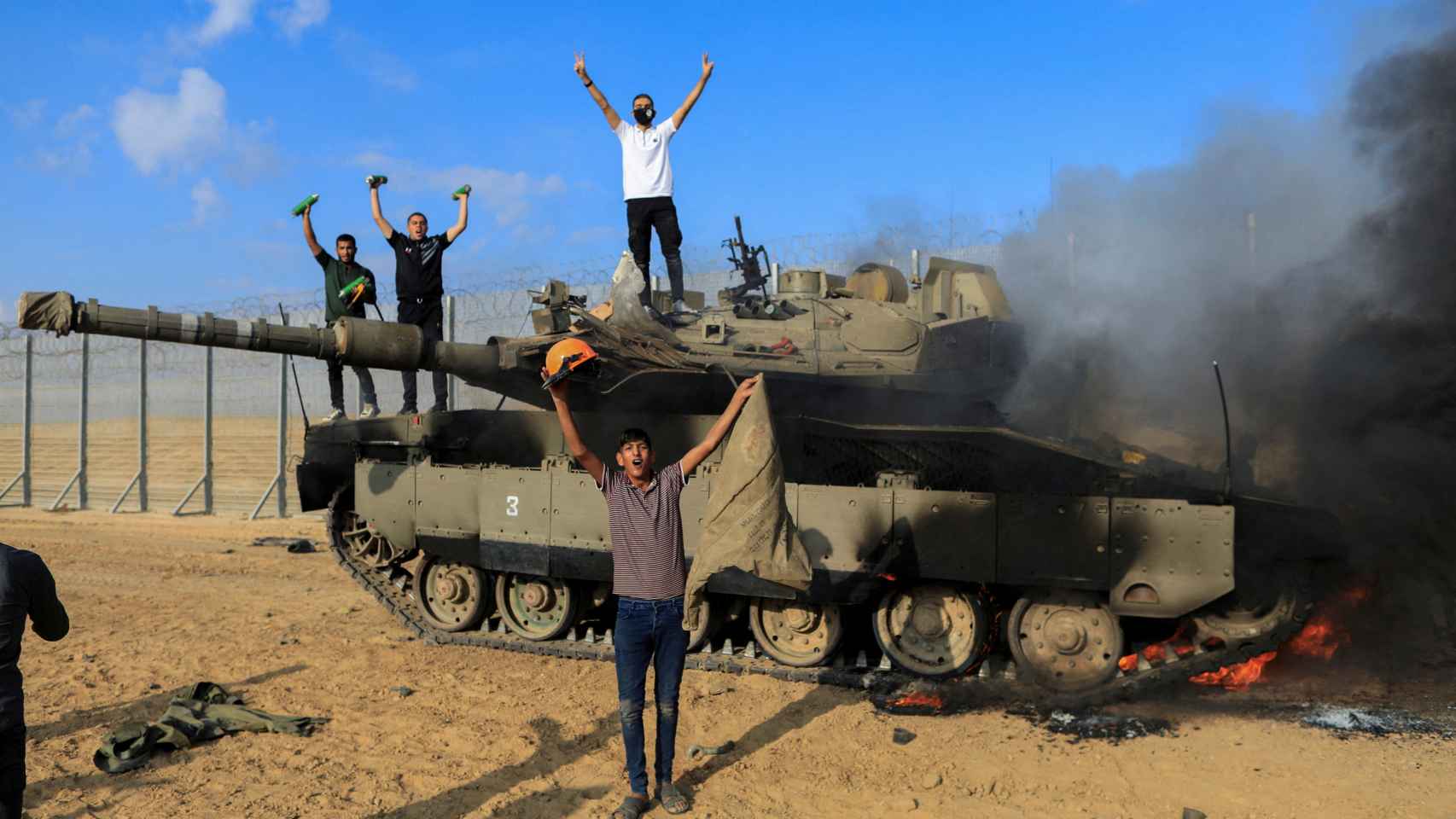 Palestinos celebran mientras un vehículo militar israelí arde después de ser atacado
