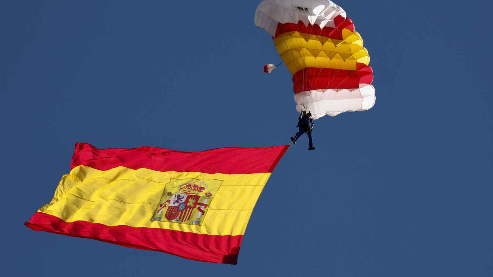 La bandera de España con uno de los miembros de la patrulla paracaídista del Ejército del Aire, durante el acto solemne de homenaje a la bandera nacional y desfile militar en el Día de la Hispanidad, a 12 de octubre de 2022, en Madrid.