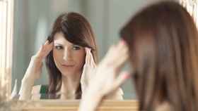 Una mujer mirando su mala cara en el espejo.