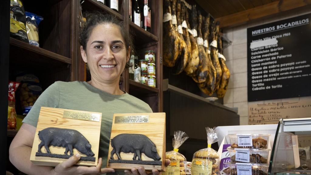 La ganadera en su tienda, con los jamones al fondo, mientras sujeta los premios obtenidos por sus cerdos.