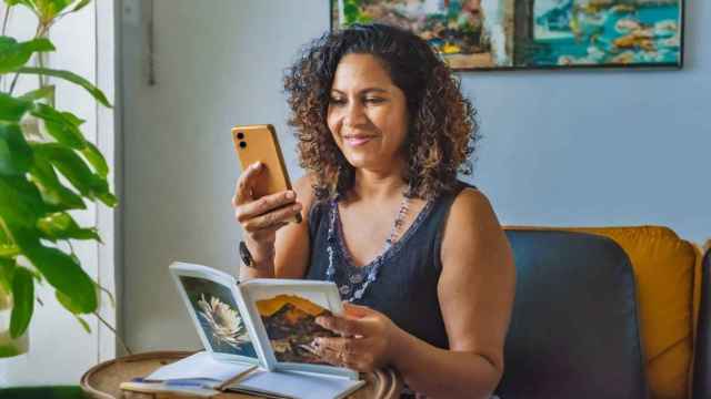Mujer mirando un móvil con un álbum de fotos en la mano