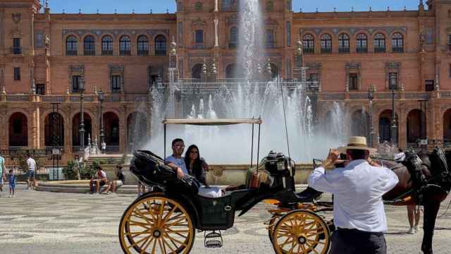 Dos turistas se hacen una foto en un coche de caballos en la Plaza de España de Sevilla.