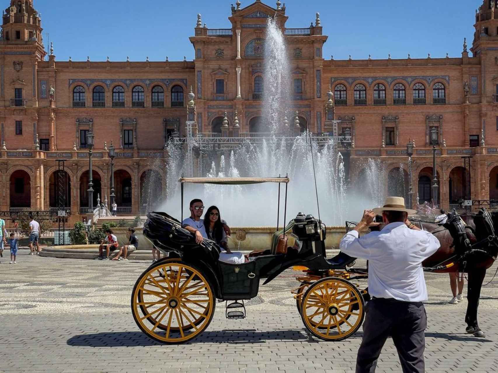 Dos turistas se hacen una foto en un coche de caballos en la Plaza de España de Sevilla.