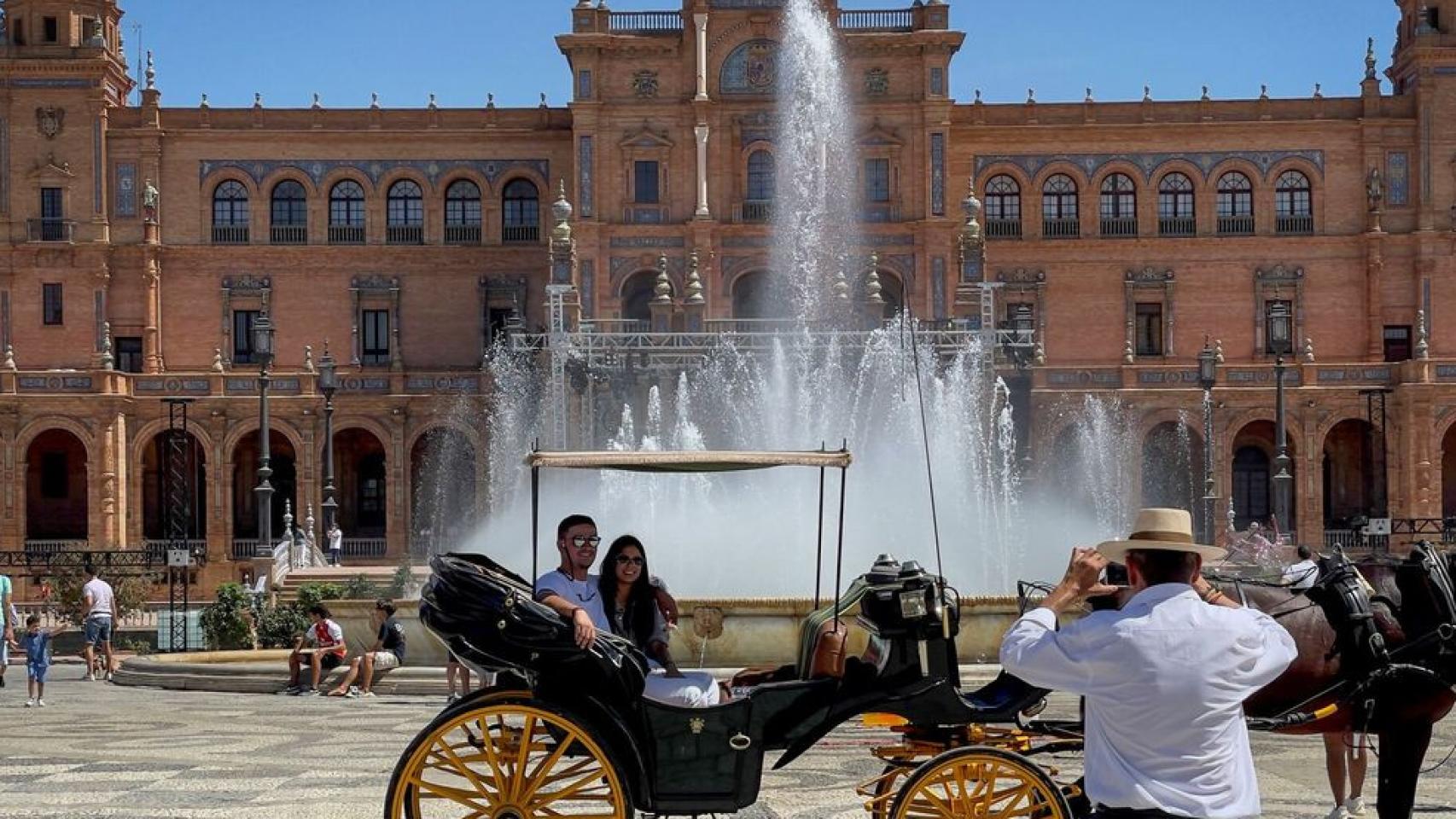 Dos turistas se hacen una foto en un coche de caballos en la Plaza de España de Sevilla.