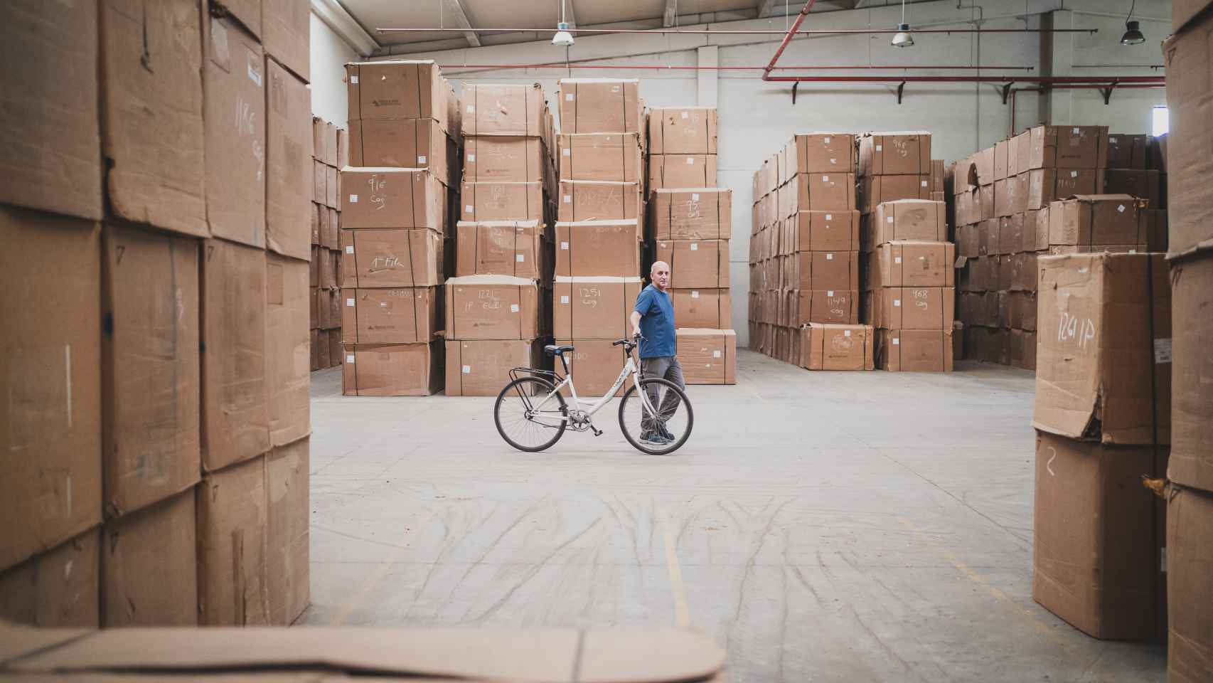José, trabajador de la cooperativa, al lado de su bicicleta; de fondo, decenas de cajas de 100 kilos cada una repletas de tabaco seco dispuesto para ser vendido a CETARSA.