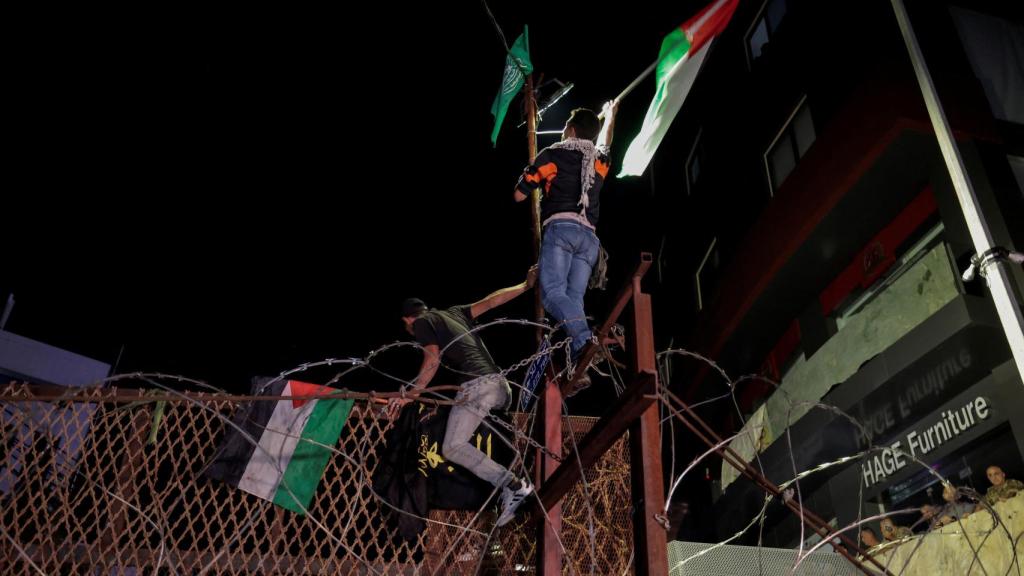 Dos manifestantes protestan con banderas palestinas mientras escalan la valla de la embajada de EEUU en Líbano.