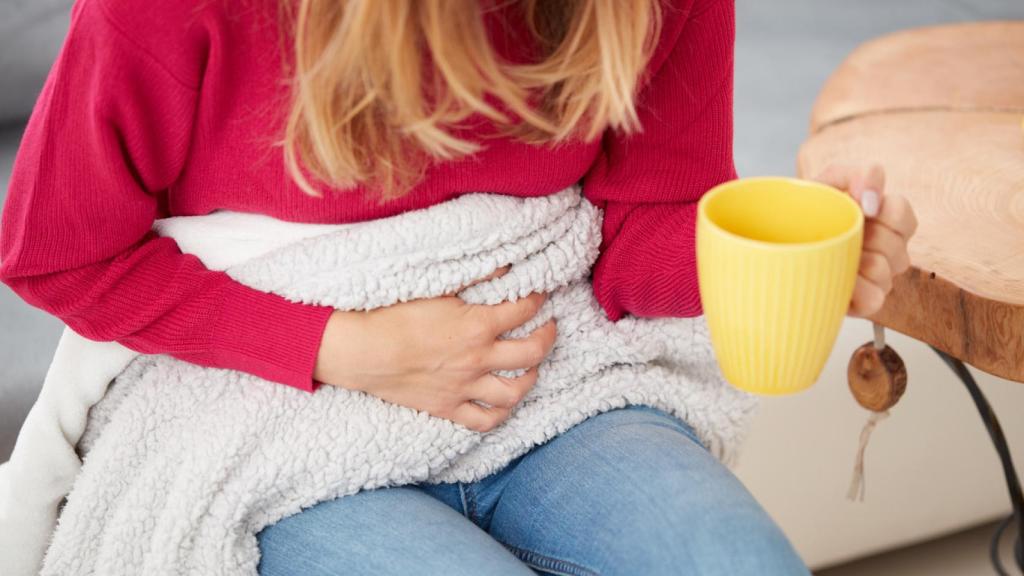 Mujer con dolores menstruales tomando té de jengibre.