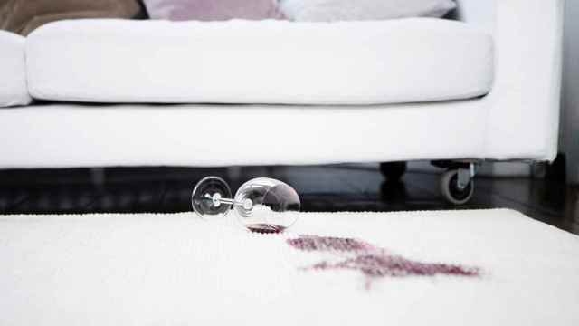 Imagen de una copa de vino derramada sobre una alfombra blanca.