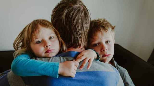 Imagen de un padre abrazando a sus hijos tristes.