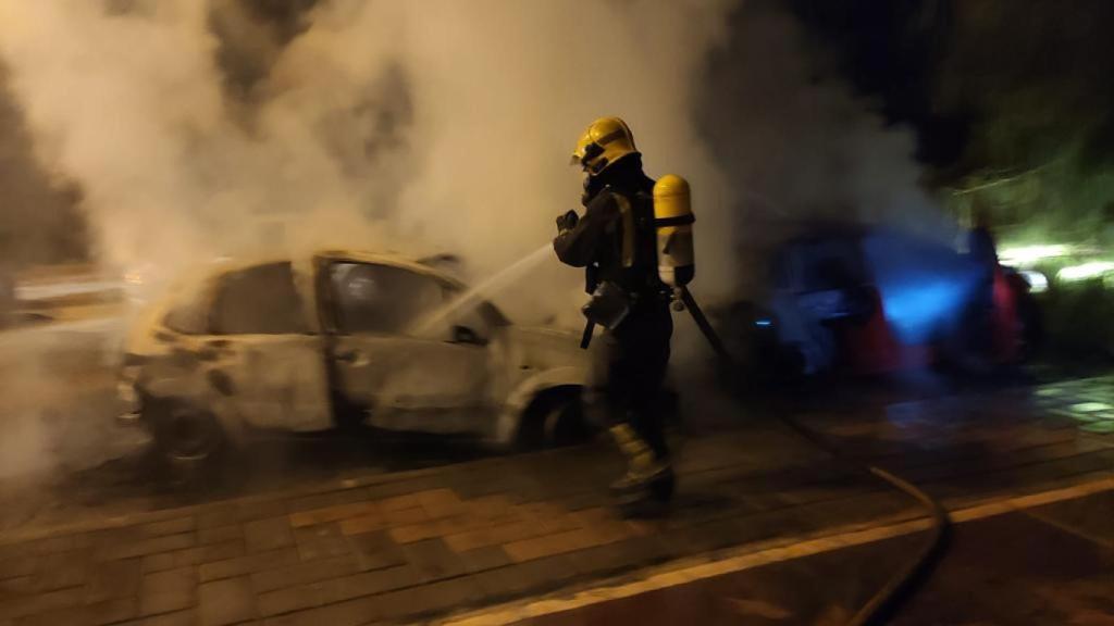 Un bombero apaga el fuego en uno de los coches afectados.