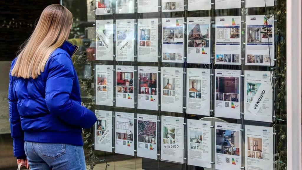 Una joven se para frente al escaparate de una inmobiliaria.