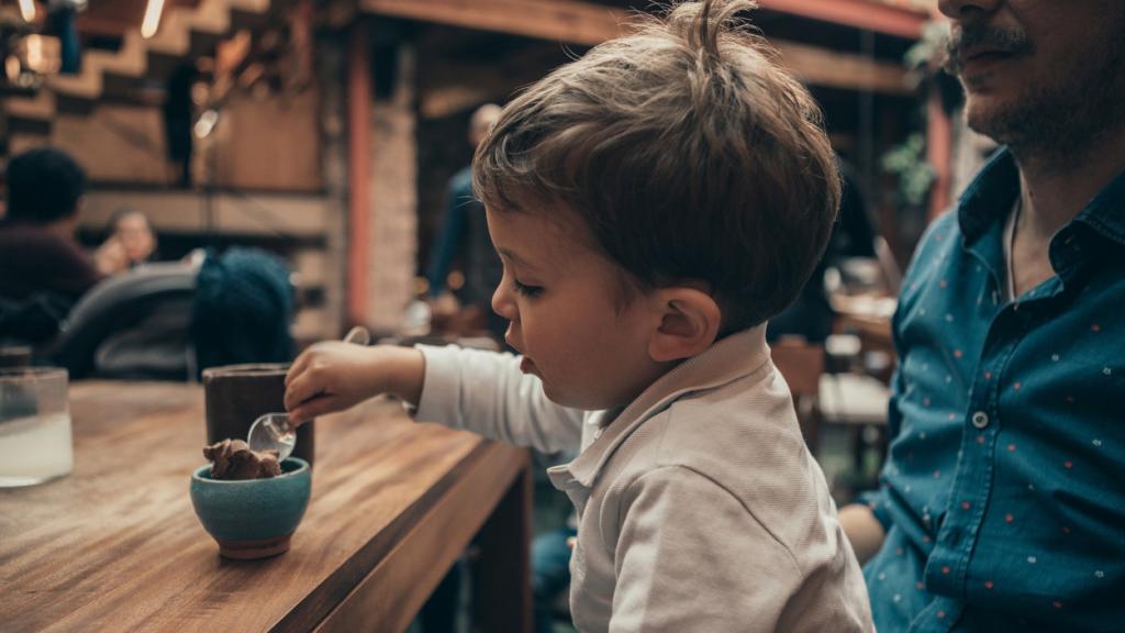 Un niño come en un restaurante junto a su padre.