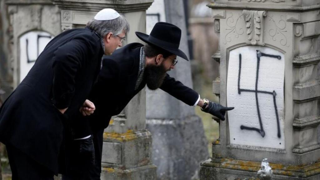 Dos hombres inspeccionan una tumba judía profanada con una esvástica en un cementerio de Estrasburgo.