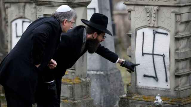 Dos hombres inspeccionan una tumba judía profanada con una esvástica en un cementerio de Estrasburgo.