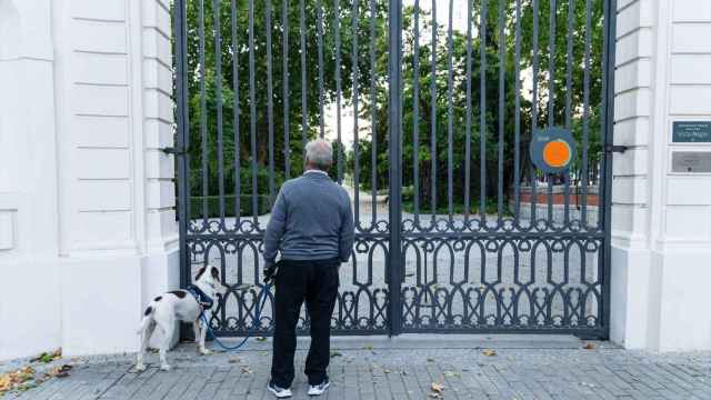 Hombre con perro mira el interior de un parque cerrado con el cartel de protocolo de alertas metereológica.
