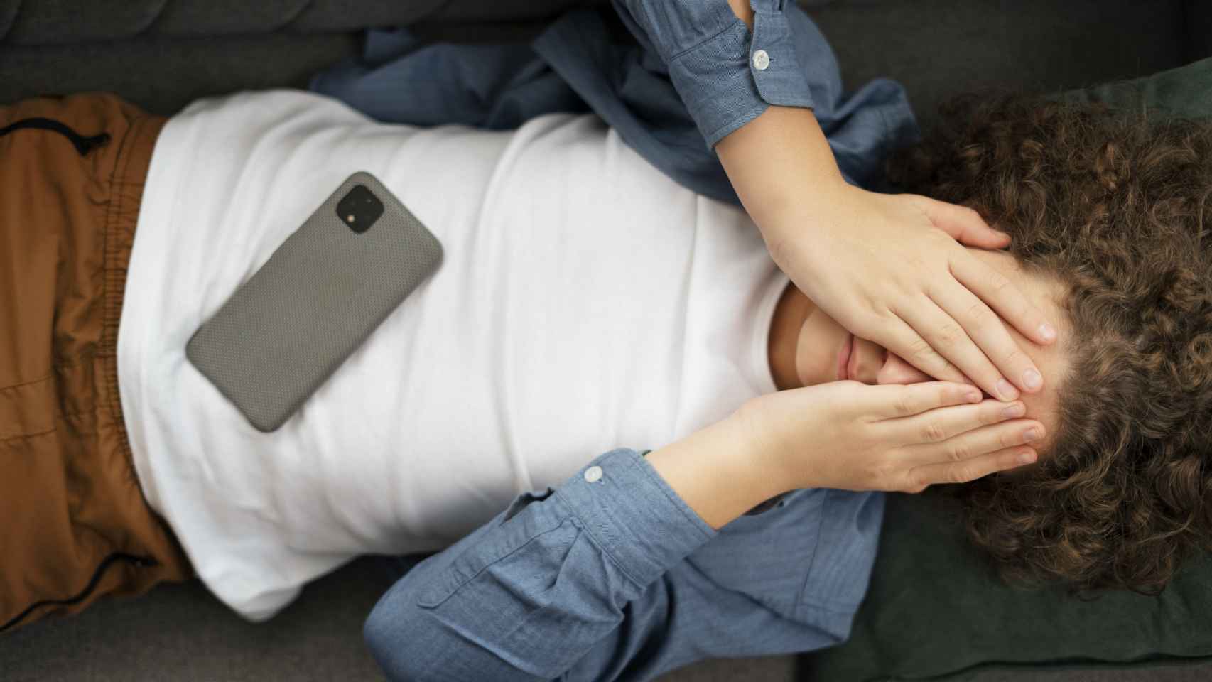 Un joven tumbado con su teléfono móvil y preocupado.