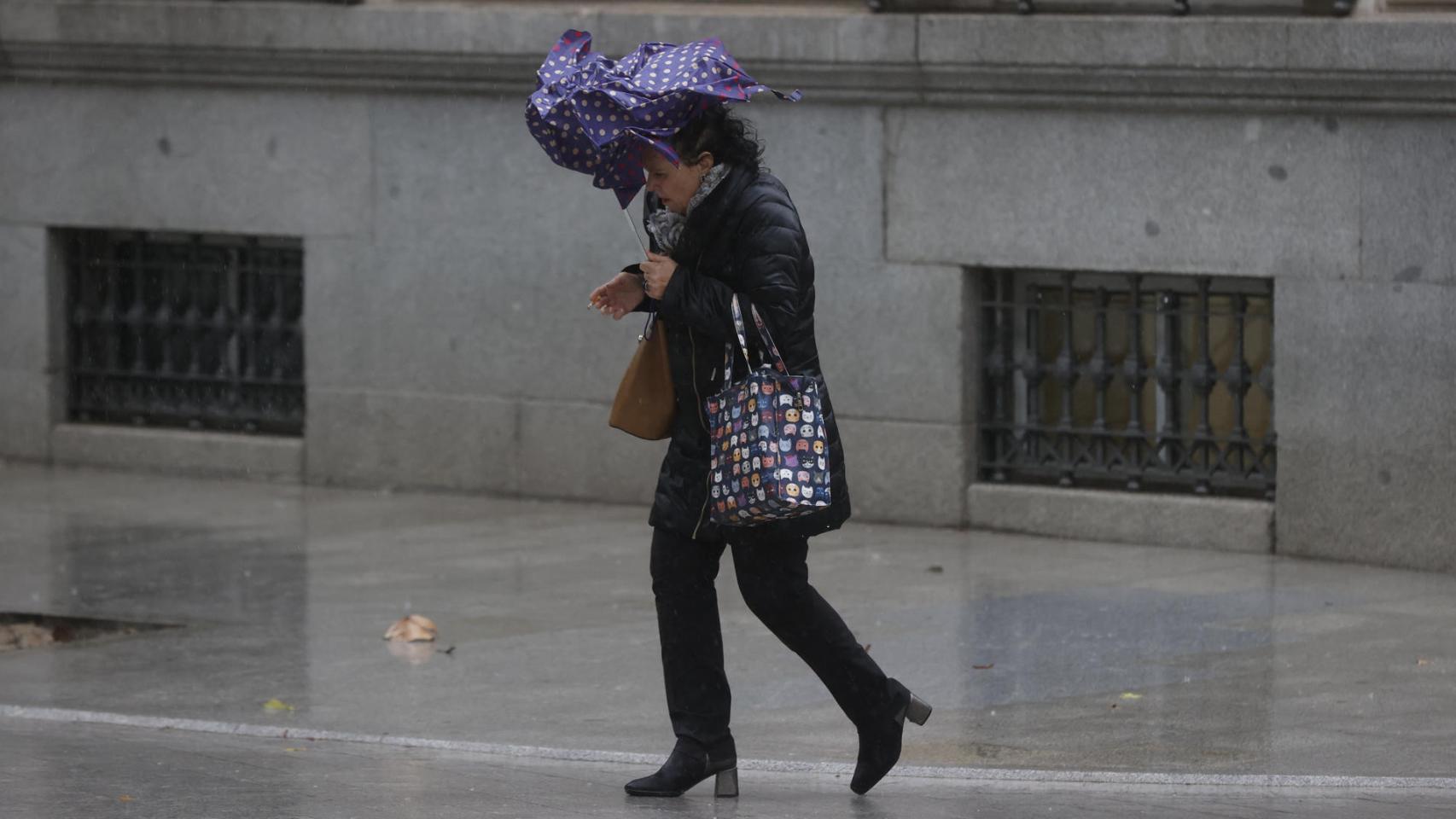 Una viandante se enfrenta a las fuertes rachas de viento mientras camina por una calle del centro de Madrid este jueves por el paso de 'Ciarán'.