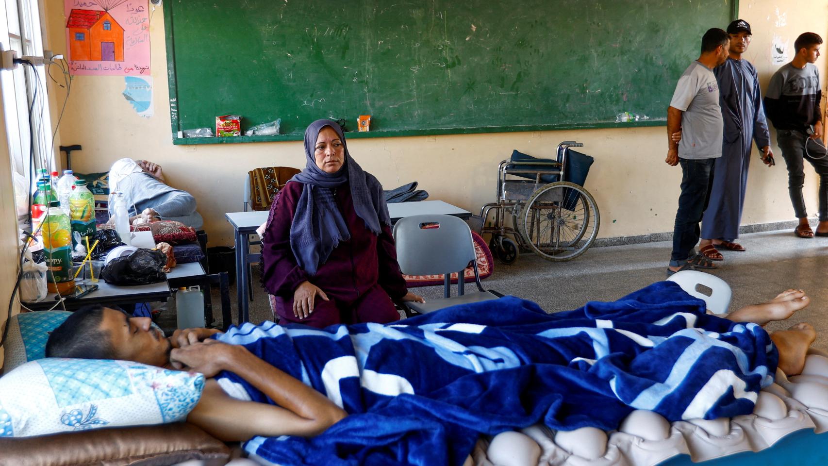 Un chico yace en una cama con su madre a su lado, en una escuela convertida en refugio de Jan Yunis (Franja de Gaza).