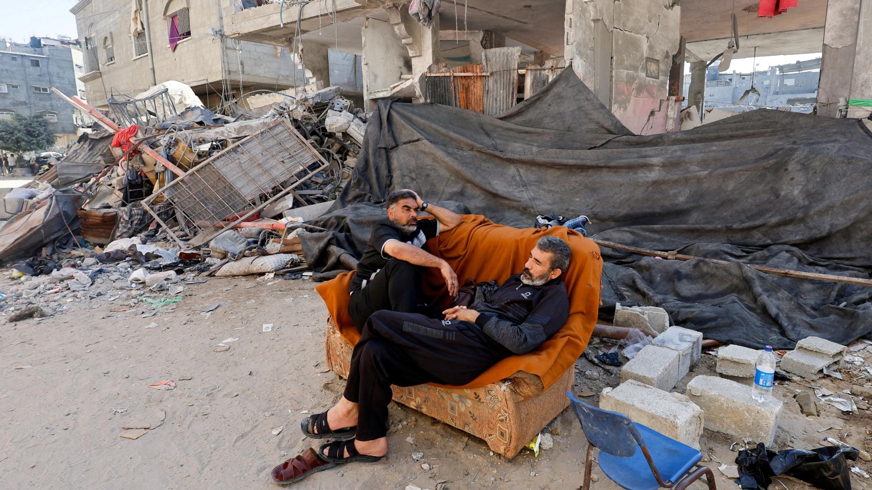 Dos hombres descansan en un sofá fuera de su edificio dañado, este martes.