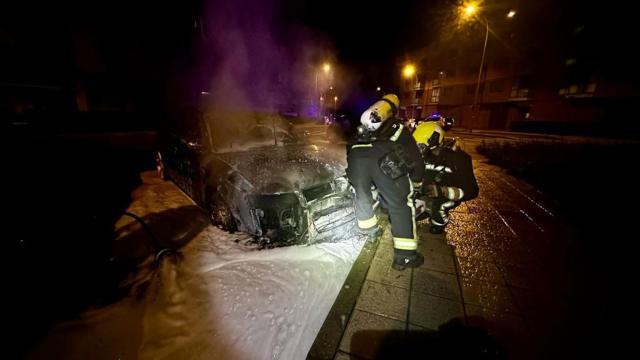 Los Bomberos de León terminando de sofocar las llamas de un coche que se encontraba en la calle aparcado