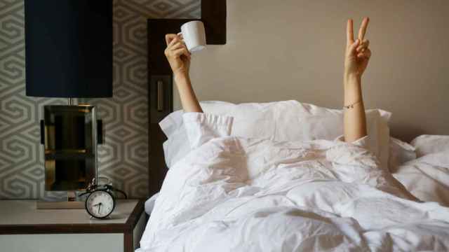 Imagen de una persona en la cama haciendo el signo de la victoria y sujetando una taza.
