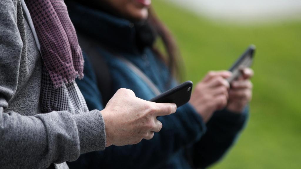 Dos personas utilizando sus teléfonos móviles.