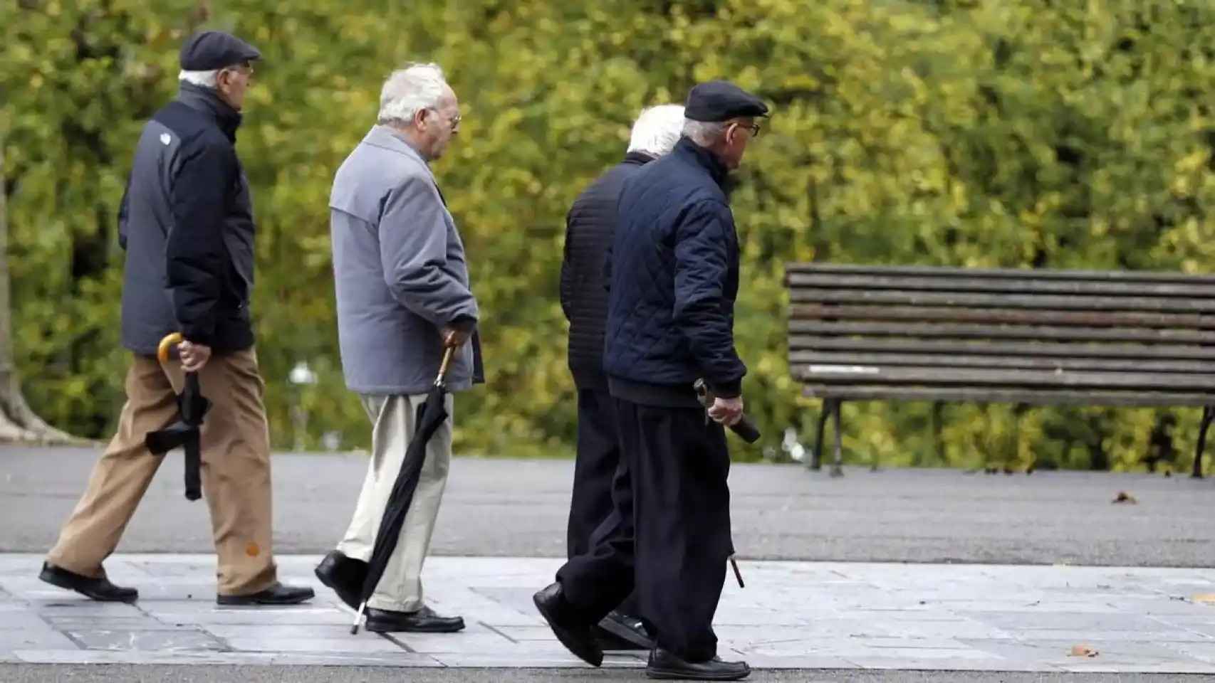 Jubilados y pensionistas dan un paseo por un parque.