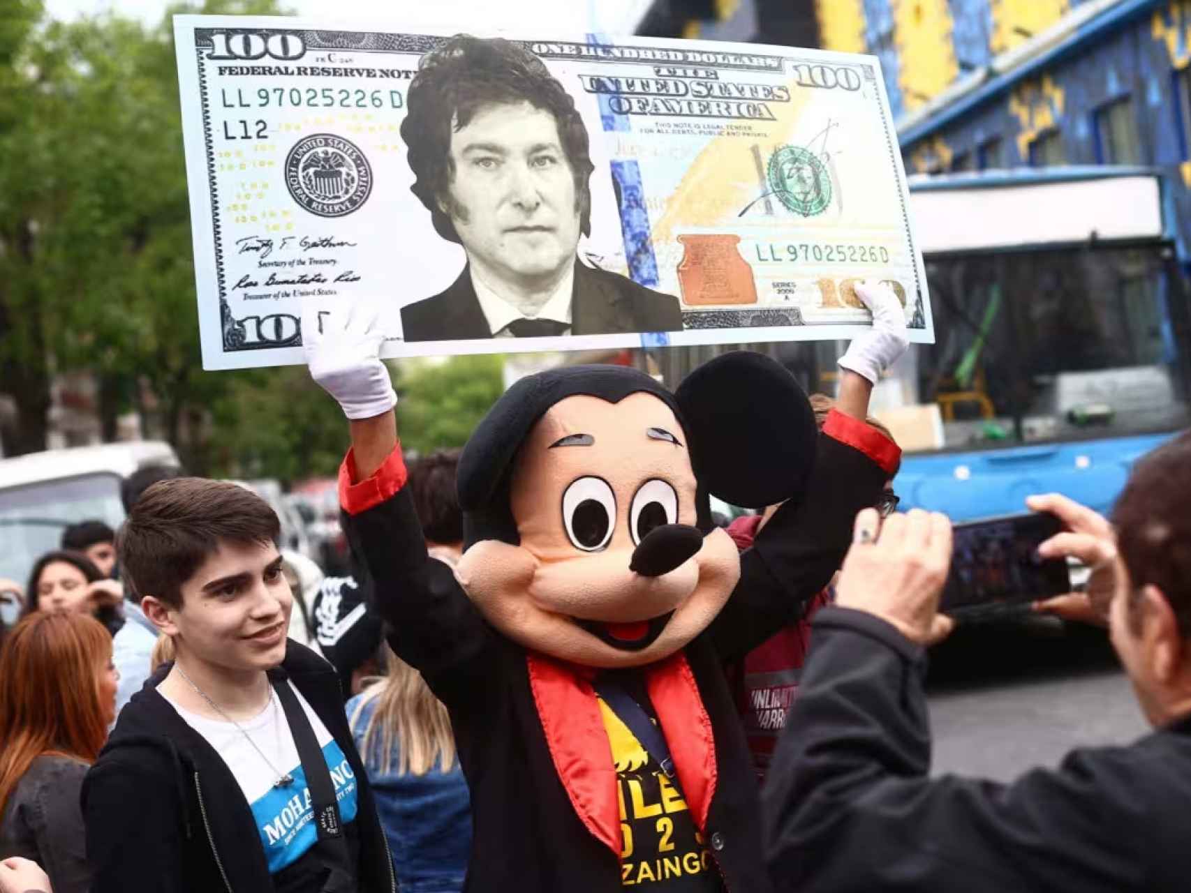 Un simpatizante de Milei disfrazado de Mickey Mouse sostiene una cartulina que representa un dólar con la efigie del candidato de La Libertad Avanza.
