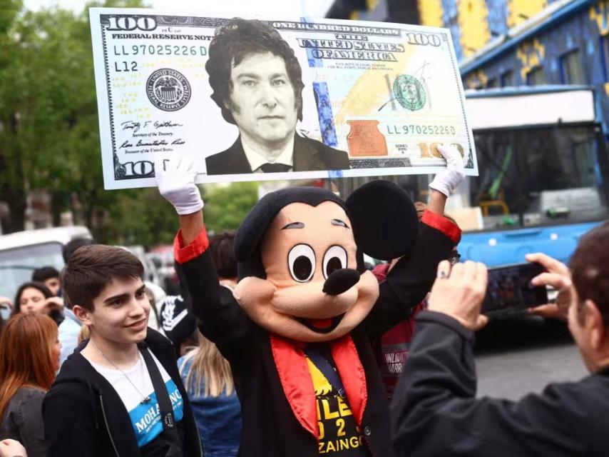 Un simpatizante de Milei disfrazado de Mickey Mouse sostiene una cartulina que representa un dólar con la efigie del candidato de La Libertad Avanza.