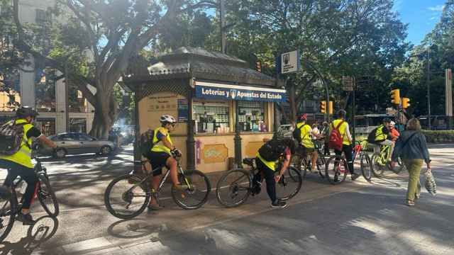 Un numeroso grupo de ciclistas en el carril bici situado a 80 centímetros de la ventanilla de esta administración de lotería.
