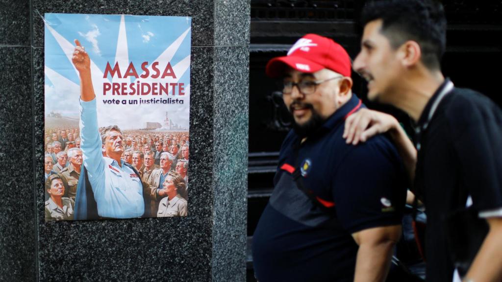 Dos hombres caminan por Buenos Aires al lado de un cartel promocional de la campaña de Massa.
