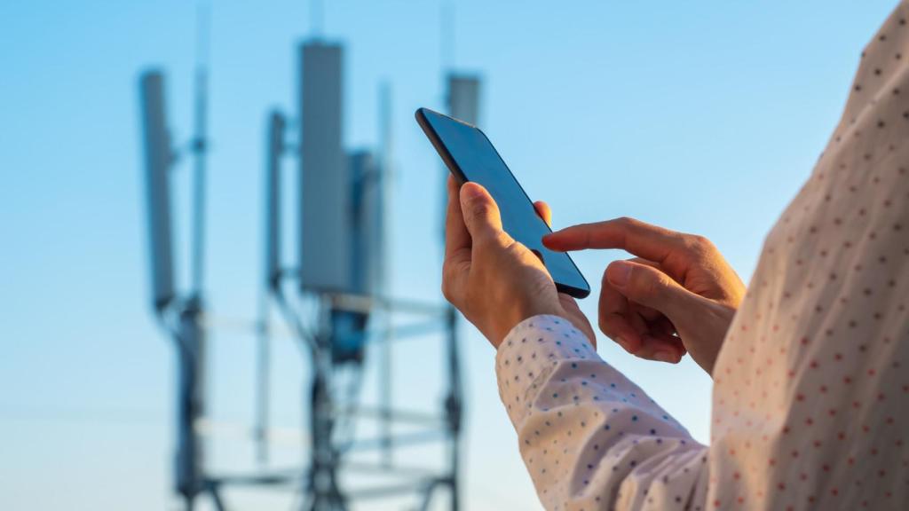 Un hombre utilizando su teléfono móvil junto a una antena de telefonía.