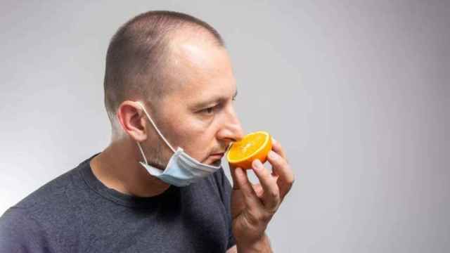 Un hombre intentando oler una naranja tras bajarse la mascarilla