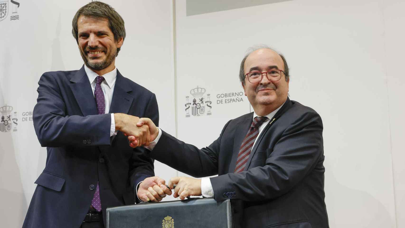 El nuevo ministro de Cultura, Ernest Urtasun (i) recibe de manos de su antecesor en el cargo, Miquel Iceta, la cartera del Ministerio de Cultura, este martes en Madrid. Foto: EFE/ Zipi