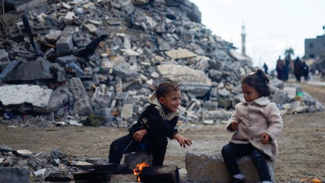 Dos niños juegan al calor del fuego junto a un edificio en escombros, este lunes en Jan Yunis.