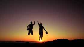 Imagen de dos personas saltando felices en una montaña al atardecer