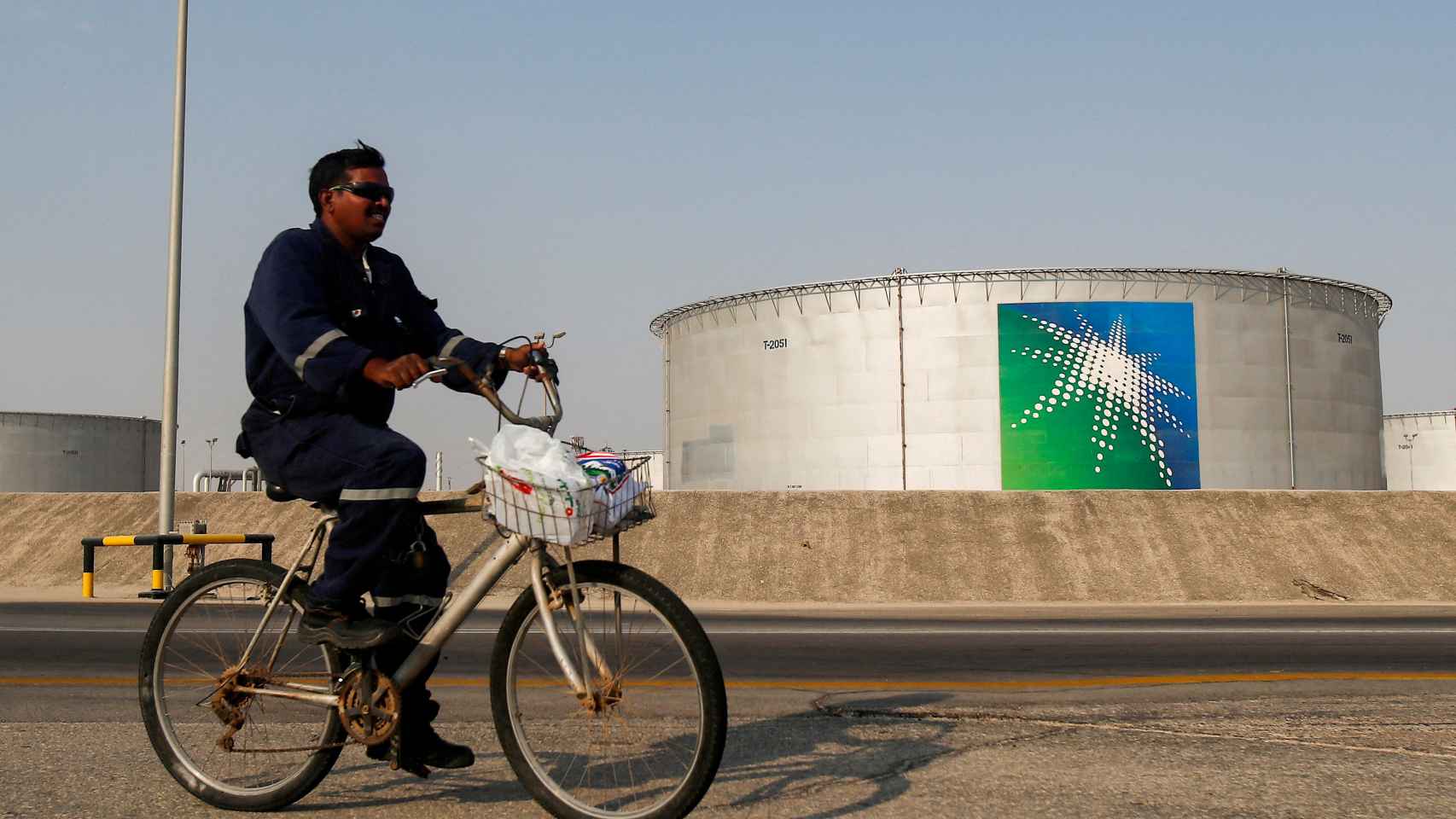 Un empleado monta en bicicleta junto a unos tanques de petróleo en las instalaciones petrolíferas de Saudi Aramco en Abqaiq.
