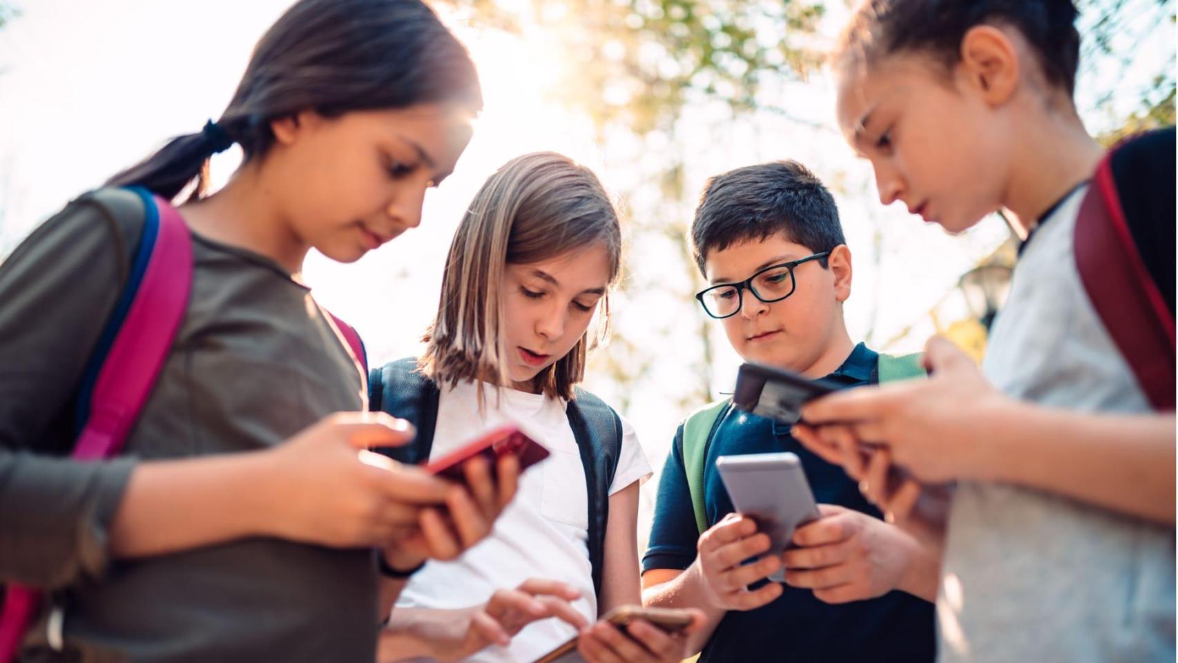 Varios niños haciendo uso de sus teléfonos móviles.