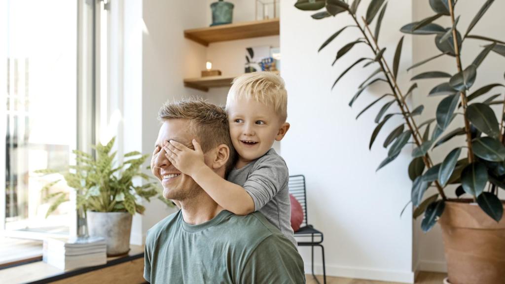 Imagen de un niño sonriente cubriendo los ojos de padre