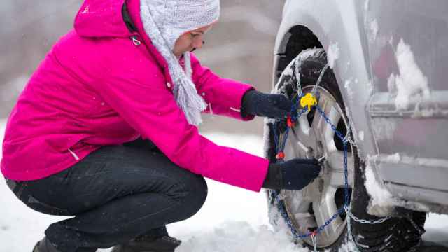 Mujer colocando unas cadenas para la nieve en el coche