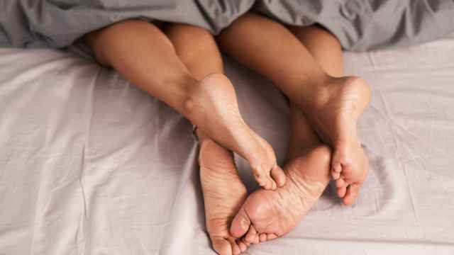 Foto de los pies de una pareja asomando desde debajo de las sábanas de la cama.