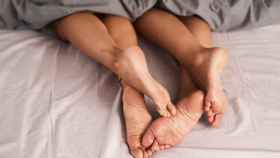 Foto de los pies de una pareja asomando desde debajo de las sábanas de la cama.