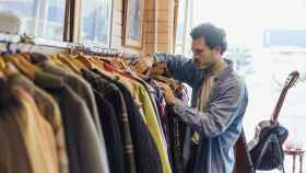 Imagen de archivo de un hombre mirando ropa en una tienda de segunda mano.