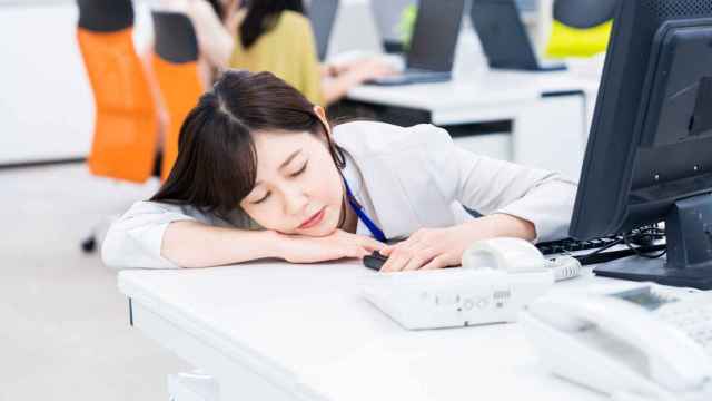 Imagen de archivo de una trabajadora de oficina japonesa dormida sobre su mesa.